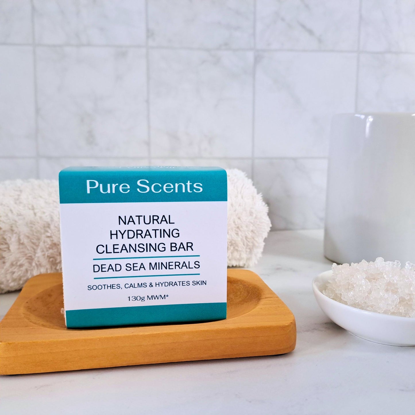 A bar of Dead Sea Salt soap sitting on a wooden soap dish surrounded by bathroom accessories with a tiled background.